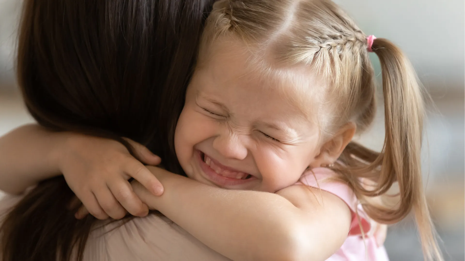 Safe, Loving Homees for Every Child A little girl hugging a women tightly with a giant smile and eyes closed shut from excitement.