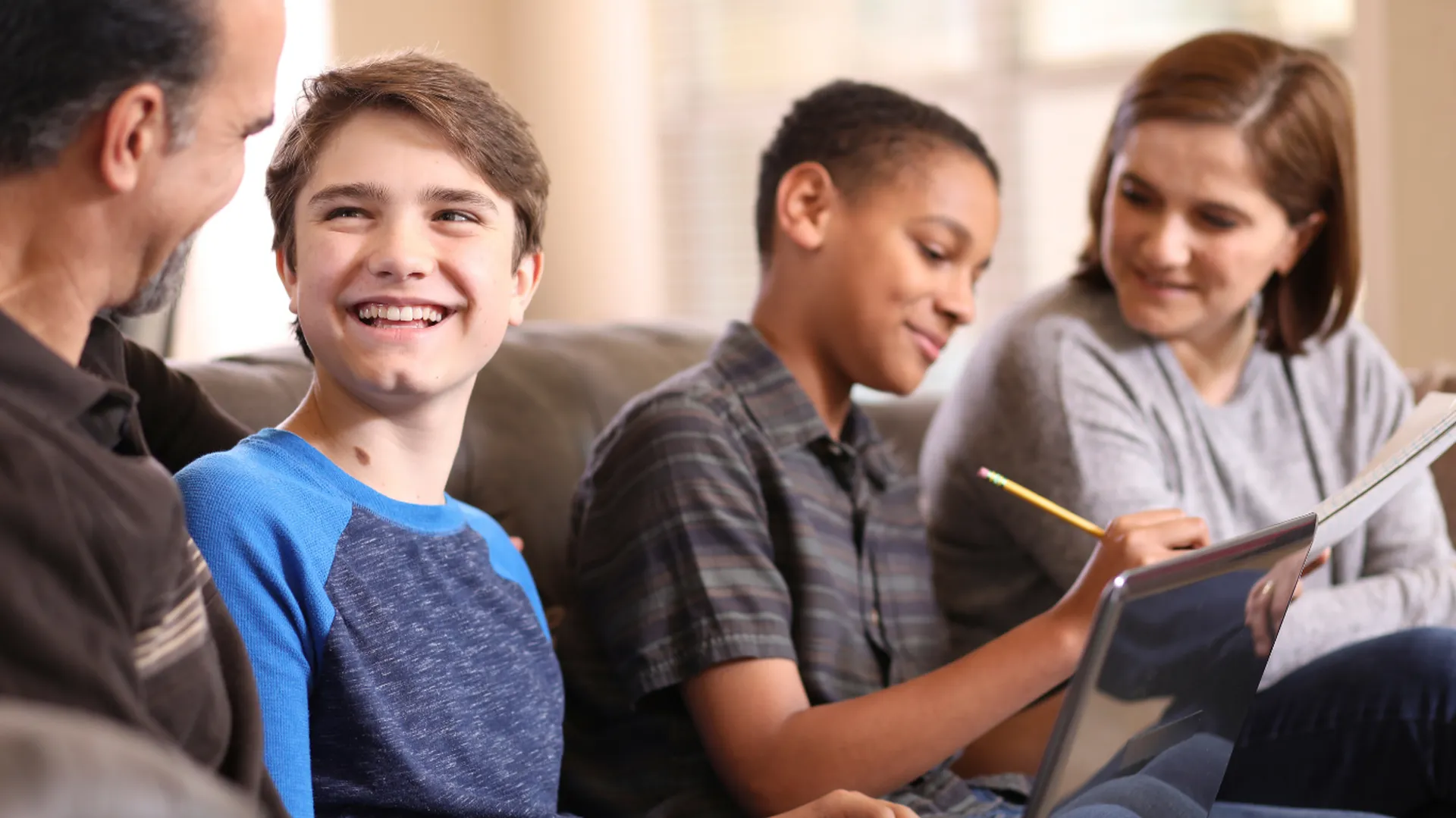 Strengthening Families, Supporting Futures Family sitting together on a couch, supporting a child learning on a laptop at home