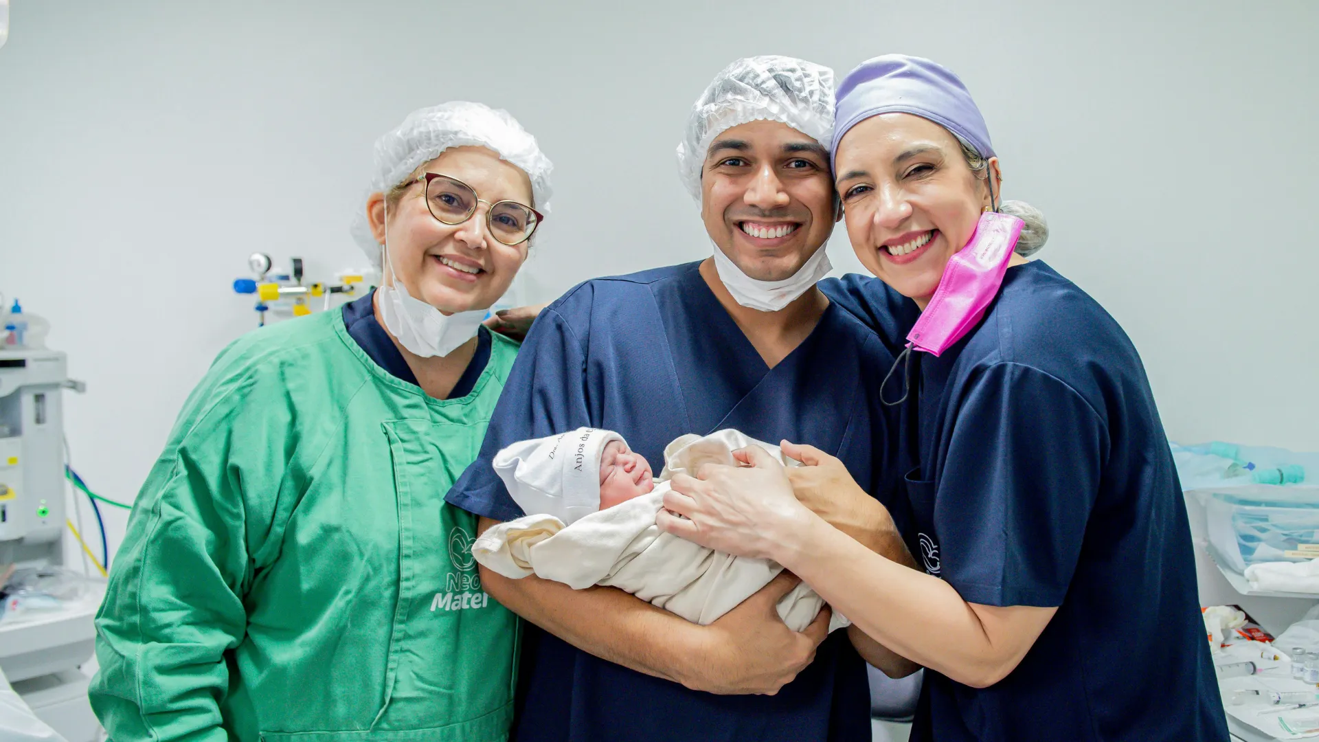 Adoptive parents and a medical professional smile while one holds a newborn baby in a hospital setting.