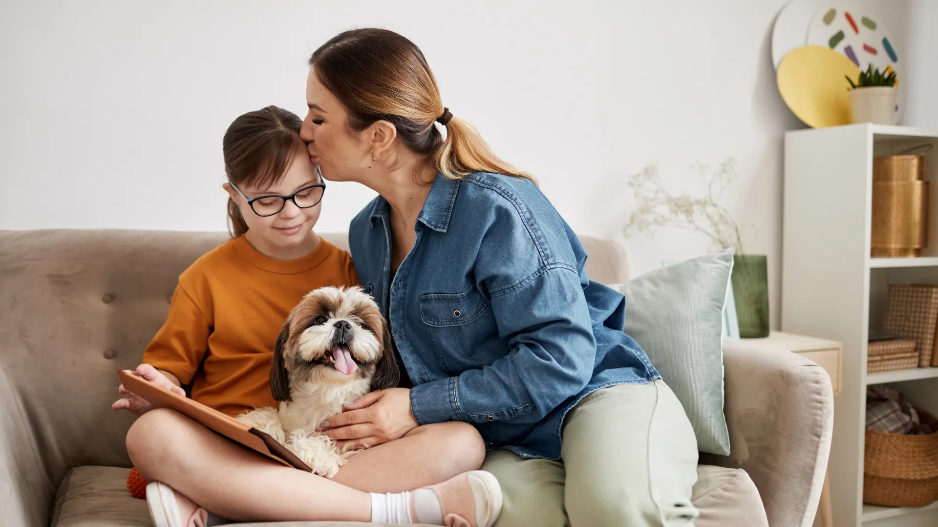 Caregiver comforting child on a couch at home while they sit with a dog and tablet