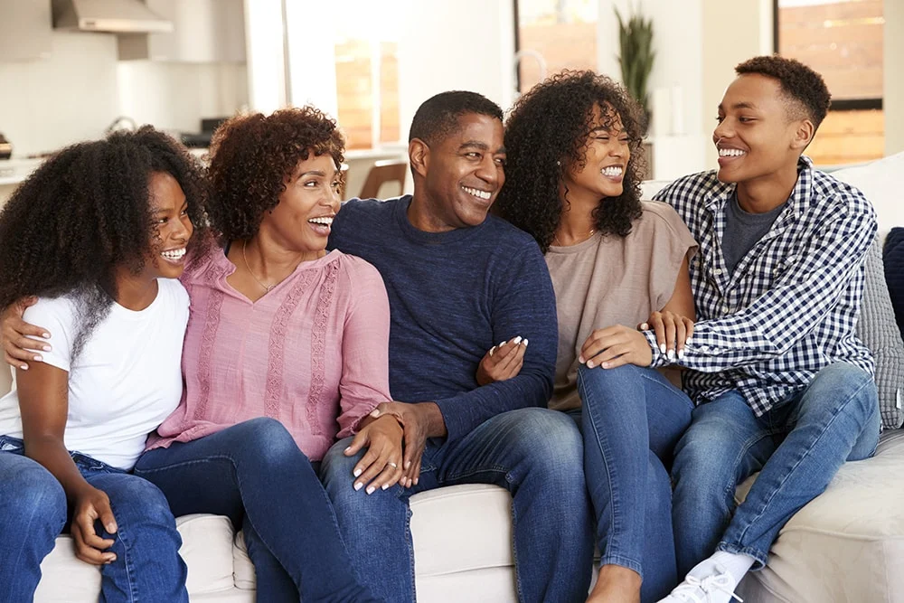 Family of five sitting on a couch, huggingly expressing laughter and joy
