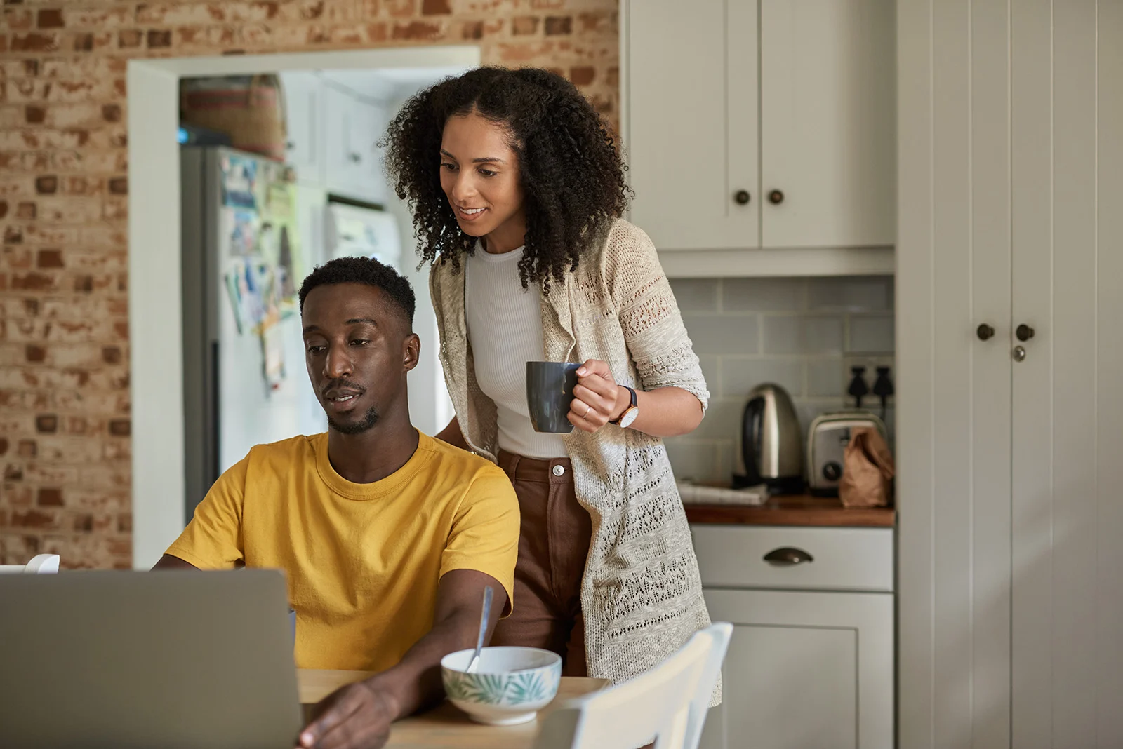 Two adults review information together on a laptop at a kitchen table.