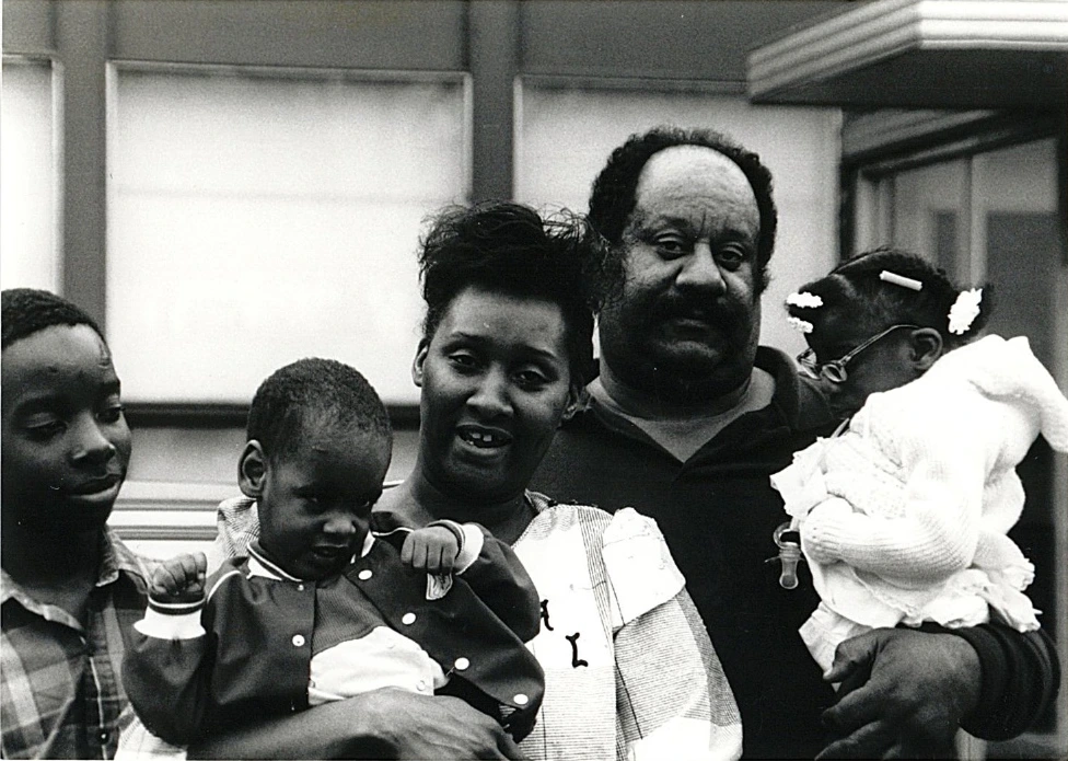 Spaulding-creating-access-where-non-existed Vintage black-and-white family portrait featuring two parents and their three children, smiling and gathered closely together outdoors.